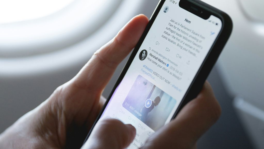 Enfoque em uma mão segurando um celular com a timeline do X aberta