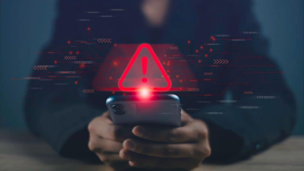 Pessoa usando celular com símbolo de atenção vermelho em cima dele