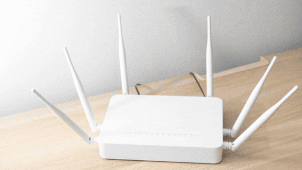 roteador branco em cima de uma mesa de madeira com uma parede cinza atrás