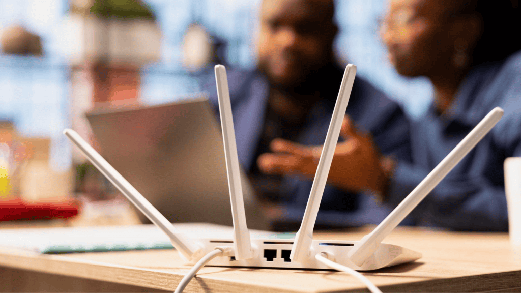 foto de um roteador em cima de uma mesa com pessoas e computadores atrás